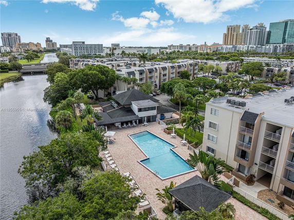 Aerial view overlooking a cityscape with several multi-story residential buildings, surrounding a large L-shaped swimming pool.