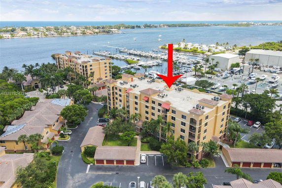 Aerial view of an apartment building with tan walls and flat roofs, located near a marina with boats docked in the water.