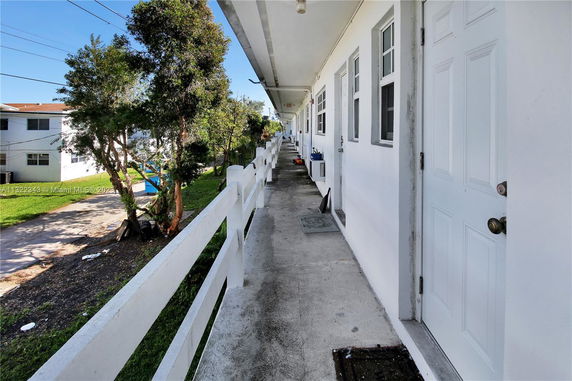 Outdoor walkway with doors leading to a residential building, showing trees and neighboring buildings.