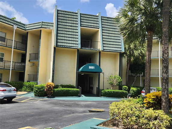 Front view of a multi-story residential building with green roofing and balconies.