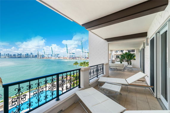 Balcony with lounge chairs overlooking the ocean and a distant city skyline.