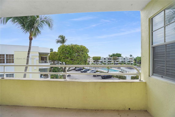View from a balcony overlooking a parking area with trees, cars, and adjacent residential buildings.