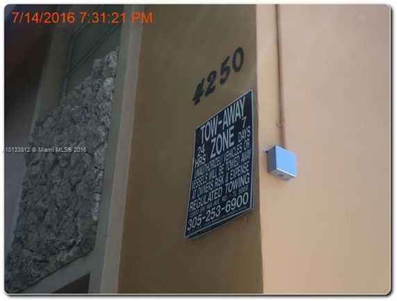 Corner view of a building with stone and plaster walls displaying an address and a tow-away zone sign.