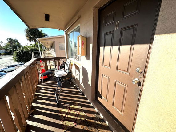 View from the balcony showing an outdoor corridor with multiple doors and a street in the background.