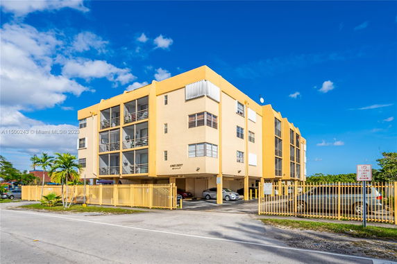 Front view of a multi-story apartment building with a gated entrance and parking area.