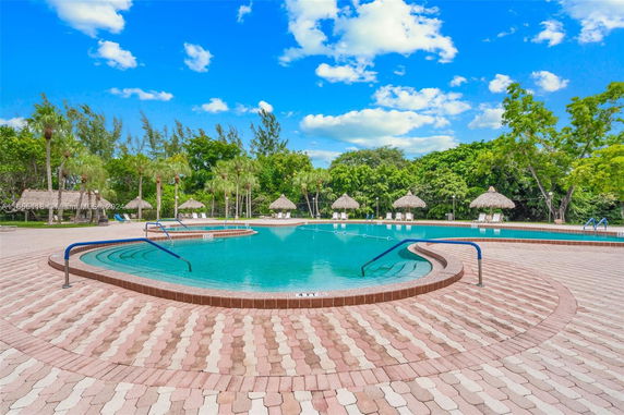 Outdoor swimming pool area with brick flooring and surrounding palm trees.