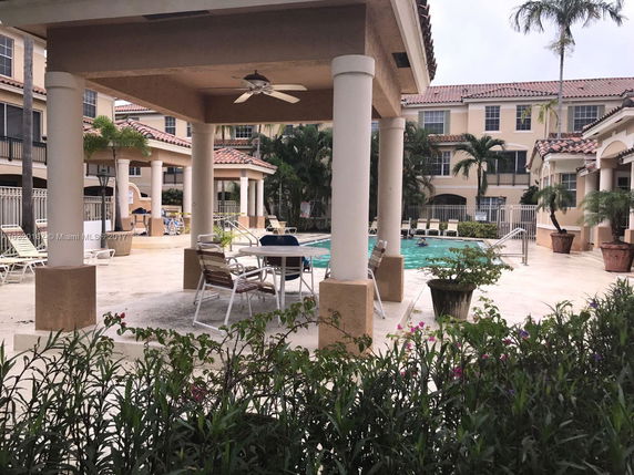 Outdoor swimming pool area surrounded by multi-story buildings with columns and seating.