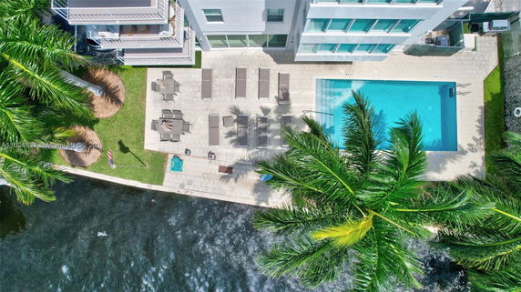 Aerial view of a swimming pool area next to a building with lounge chairs and patio furniture.