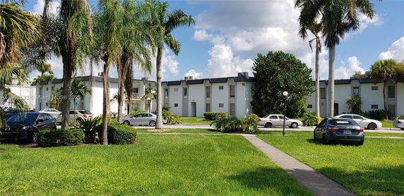 Front view of a multi-story building with palm trees and parked cars.