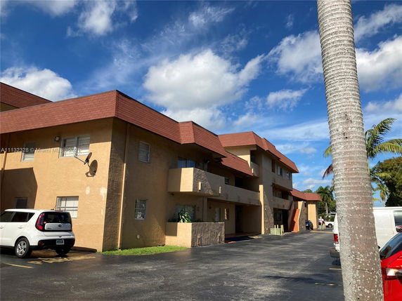 Front view of a multi-story building with a brown roof and a parking area in front.