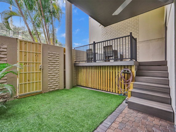 Outdoor area with artificial grass, a wooden gate, and a small elevated deck with seating.