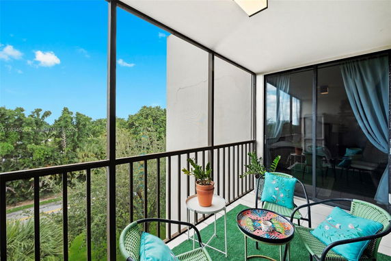 View from a balcony with outdoor furniture and a railing, overlooking trees.