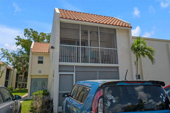 Front view of a two-story building with a red tile roof and a screened upper balcony.