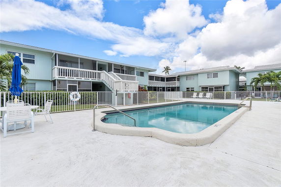 Outdoor swimming pool area in front of a two-story building with balconies.