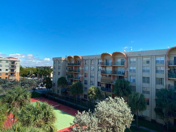 View of a multi-story residential building with balconies and a tennis court in the foreground.