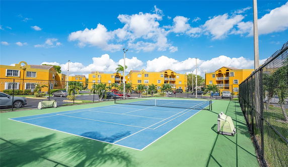 Tennis court adjacent to yellow residential buildings.