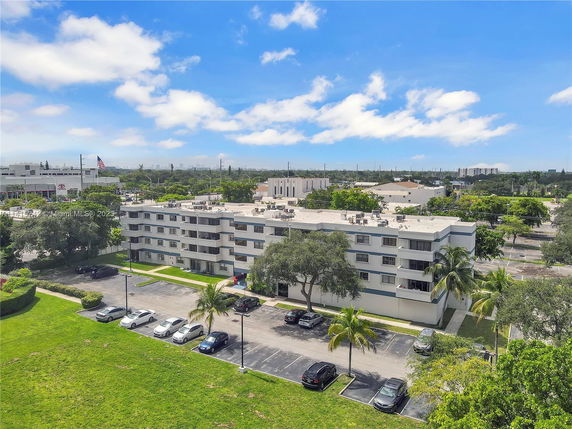 View of a multi-story apartment building with surrounding parking and greenery.