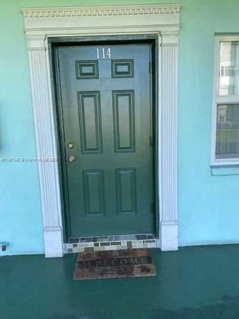 Front view of a building entrance with a green door and a welcome mat.