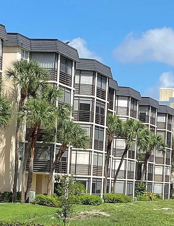 Front view of a multi-story apartment building with balconies and palm trees.