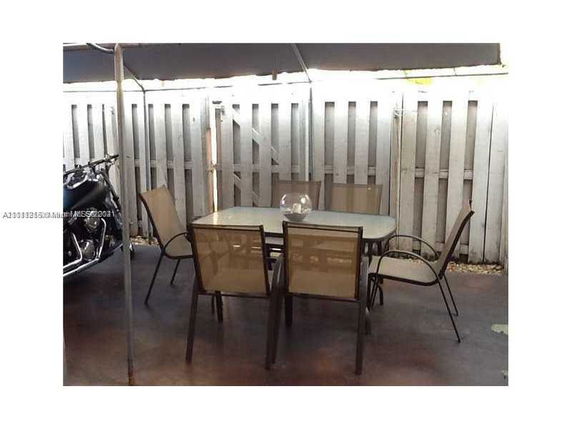 Outdoor patio area with table and chairs near a fence and motorcycle.