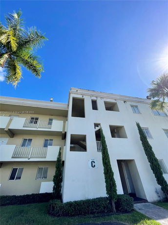Front view of a multi-story building with balconies and bushes in front.
