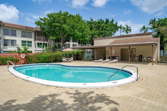 Outdoor swimming pool area with surrounding chairs and nearby building.