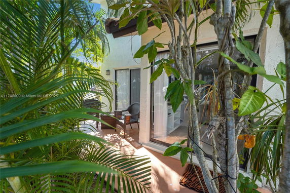 Outdoor view with a partial glimpse of a house and patio area surrounded by lush greenery.
