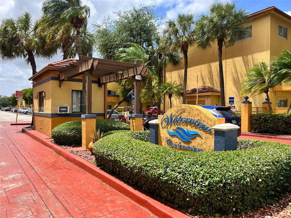 Front view of a condominium building with a prominent sign and tropical landscaping.
