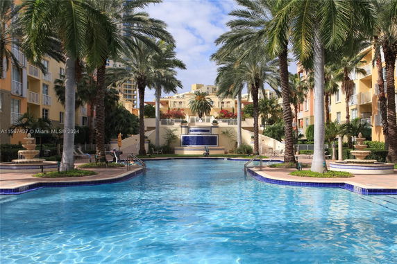 Outdoor swimming pool area surrounded by palm trees and buildings.
