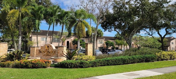 Front view of a residential building with palm trees and a stone sign in the foreground.