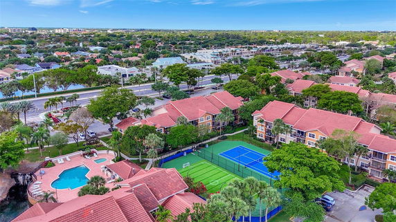 Aerial view of residential area with red-roofed buildings, tennis courts, and a swimming pool.