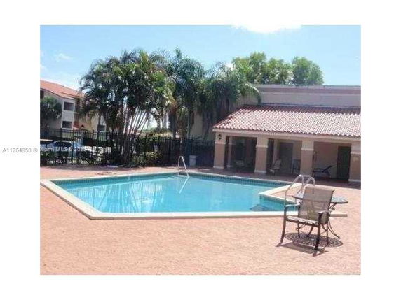 Outdoor swimming pool area with a nearby building and palm trees.