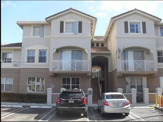 Front view of a multi-story residential building with balconies and parking area.