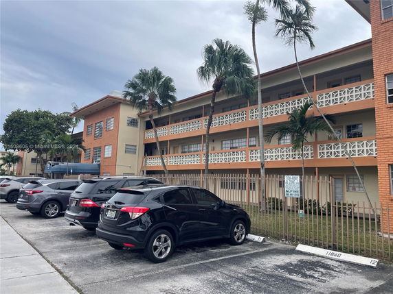 Parking area in front of a three-story building with palm trees.