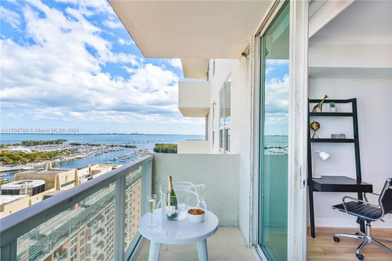 View from a high-rise building balcony overlooking a marina and body of water, with a partial interior view of an office space.