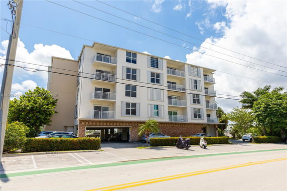 Front view of a multi-story residential apartment building with balconies and ground-level parking.