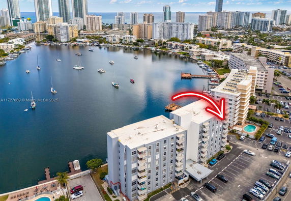 Aerial view of waterfront residential buildings with a lake and boats, surrounded by high-rise structures.