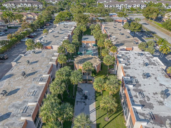 Aerial view of multiple flat-roofed buildings with rooftop equipment and surrounding palm trees.