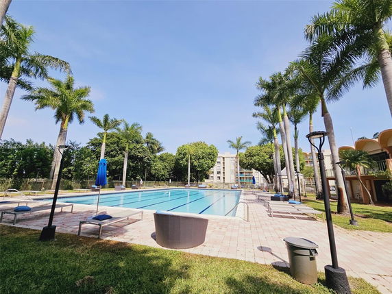 Outdoor swimming pool area with surrounding lounge chairs and palm trees.