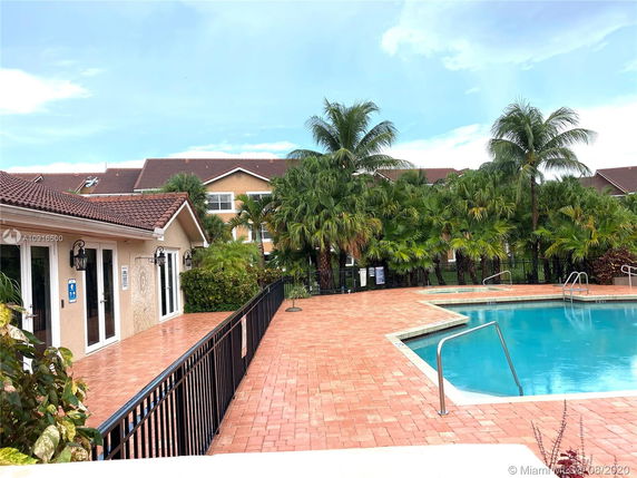 View of a swimming pool with adjacent building and palm trees.