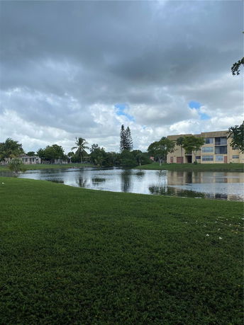 View of a body of water with buildings and trees in the background under a cloudy sky.