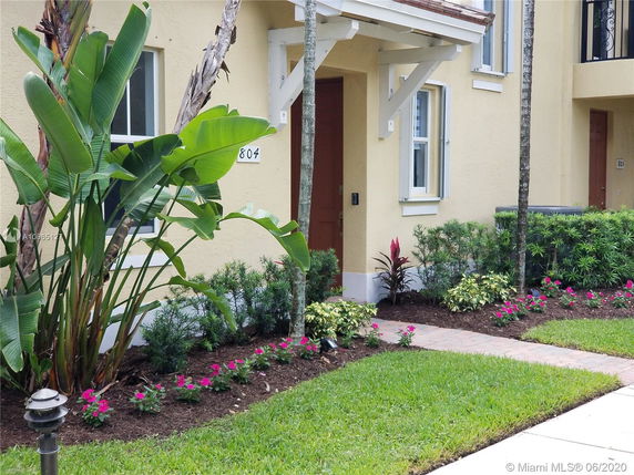 Front view of a yellow two-story townhouse with a small garden in front.