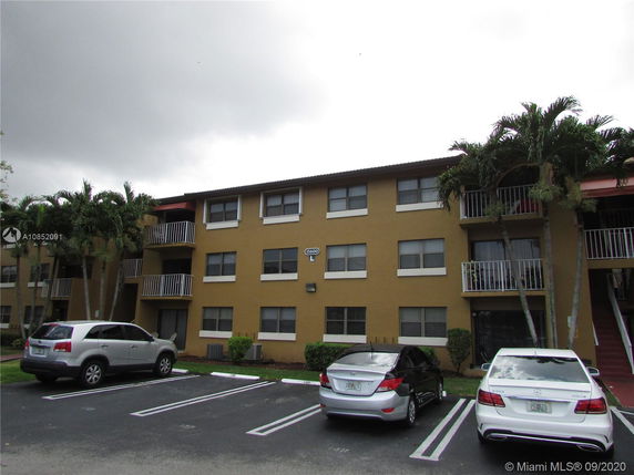 Front view of a three-story apartment building with balconies and parking area.