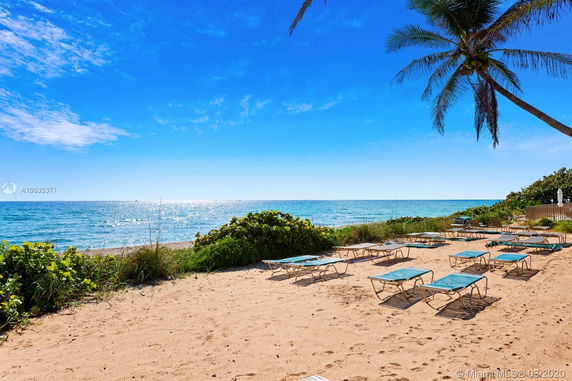 Sandy beach with lounge chairs under a clear blue sky, overlooking the ocean.