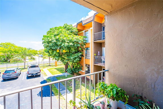 View of a parking area and neighboring building from a balcony with potted plants.