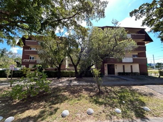 Front view of a multi-story building with balconies and trees in front.