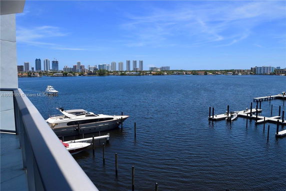 Panoramic view from a building showing a waterfront with docked boats and a city skyline in the distance.
