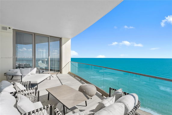 Balcony view with ocean in the background, featuring modern outdoor furniture and glass railing.