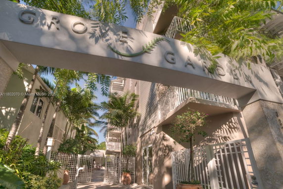 Front view of a multi-story building with a gated entrance and lush greenery.