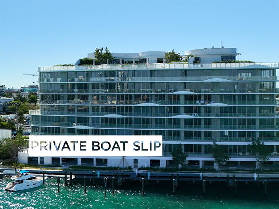 Front view of a multi-story waterfront building with large glass windows and greenery on the rooftop.
